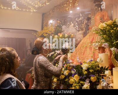 Eine Trans-Preisträchtigkeit bläst Rauch auf eine Statue von Santa Muerte in einem Heimattempel in Queens, New York City. Stockfoto