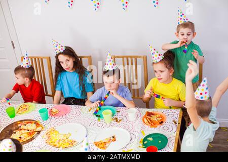 Kinder feiern Geburtstag mit einer Pizza im Café. Geburtstagsfeier. Süße Kinder in Geburtstagshüten, die zusammen Spaß haben Stockfoto