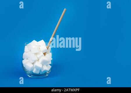 Weiße Zuckerwürfel in einem Glas mit Strohhalm und auf blauem Grund Stockfoto