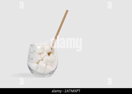 Weiße Zuckerwürfel in einem Glas mit Strohhalm und grauem Hintergrund Stockfoto