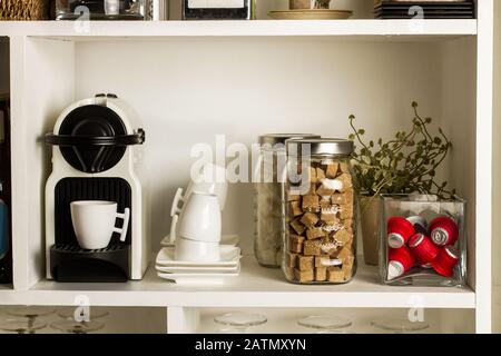 Kaffeemaschine, weiße Tassen und braune und weiße Zuckerwürfel in weißen Regalen Stockfoto