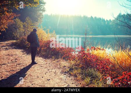 Man Tourist steht am Herbstmorgen auf einem malerischen Seeufer und blickt auf den Sonnenaufgang Stockfoto