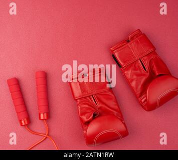 Paar Boxhandschuhe aus rotem Leder und rotes Springseil auf Neopren-Matte, Sportset, Draufsicht Stockfoto