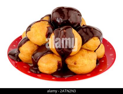 Platte aus cremefarbenen Profiterolen mit Schokoladenganachesauce, die isoliert auf weißem Grund übergossen wurde Stockfoto