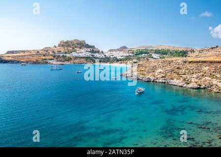 Boote ankerten auf dem Meer in der Nähe des Dorfes Lindos, Akropolis von Lindos im Hintergrund (Rhodos, Griechenland) Stockfoto