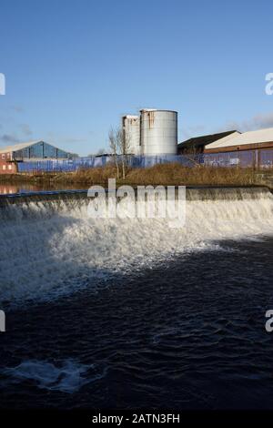 Weir am Fluss irwell mit Industriegebäuden und Silos im Hintergrund in radcliffe, Bury lancashire UK Stockfoto