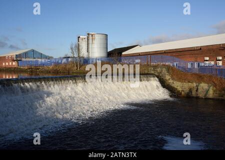 Weir am Fluss irwell mit Industriegebäuden und Silos im Hintergrund in radcliffe, Bury lancashire UK Stockfoto