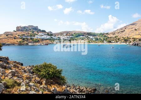 Bucht von Lindos mit Booten, weißen Häusern des Dorfes Lindos und Akropolis im Hintergrund (Rhodos, Griechenland) Stockfoto