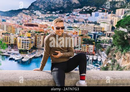 Junger Mann, der auf dem Seebrücke in Monaco sitzt und vom Prinzenpalast in Monte Carlo an der französischen Riviera aus einen Panoramablick bietet. Monaco Ville Harbour, F. Stockfoto