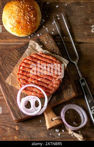 Frische, hausgemachte Burger auf wenig Schneidbrett und rohen Schnitzel und in Scheiben geschnittene Zwiebel, serviert mit Ketchup Soße und Fleisch Gabel über Holz- Tabelle. Dunklen rustikalen Stockfoto