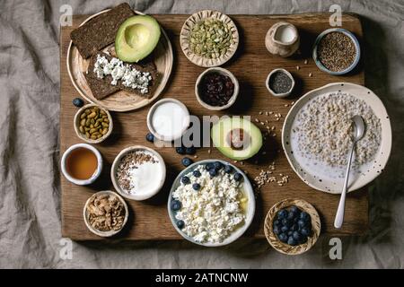 Gesundes Frühstück. Verschiedene Frühstücksgerichte Weizen, Joghurt, Kefir, Hüttenkäse, Avocado, Roggenbrot, Samen, Nüsse und Beeren im Keramiksortiment Stockfoto