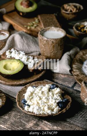 Gesundes Frühstück. Verschiedene Frühstücksküche mit gerountem Weizen, Joghurt, Kefir, Hüttenkäse, Avocado, Roggenbrot, Samen, Nüssen und Beeren Sortiment i Stockfoto