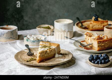 Käsekuchen mit verschiedenen Belägen auf Keramikplatten und verschiedene Soßen in Keramikschalen auf weißem Tischtuch. Dessert zum Frühstück Stockfoto