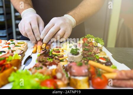 Nahaufnahme des Chefkochs bei der Zubereitung von Buffetmahlzeiten zeigen Fingerfood auf Papierplatten. Stockfoto