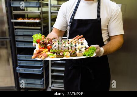 Küchenchef oder Kellner, der eine Platte voller frischer Häppchen hält, Snacks für Buffetmahlzeiten im Restaurant. Stockfoto