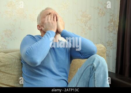 Junger Mann in einem blauen Pullover mit Kopfschmerzen zu Hause auf der Couch sitzen Stockfoto