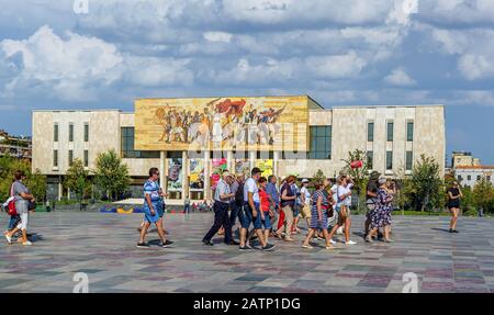 Touristen marschieren auf dem Skanderbeg-Platz vor dem nationalen Geschichtsmuseum. Das Mosaik über dem Museum nannte Die Albaner, die die Geschichte der natio erzählen Stockfoto