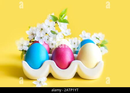 Bunte gelbe Eier mit Frühlingsblumen in Porzellanbox auf Gelb. Ostern. Frühling. Nahaufnahme. Stockfoto