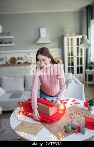 Dunkelhaarig mit rotem Papiermädchen in einem rosafarbenen Hemd, das einen Geschenkkasten bedeckt Stockfoto