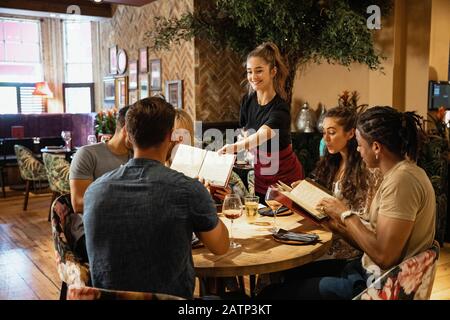 Eine multiethnische Gruppe von Freunden, die in einem Restaurant zusammen Menüs betrachten, die ihnen von einer Kellnerin gegeben wurden. Stockfoto