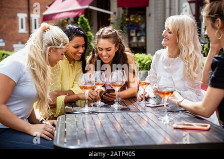 Eine Gruppe weiblicher Freunde, die im Sommer zusammen im Freien trinkt. Sie sehen sich das Telefon einer Frau an. Stockfoto