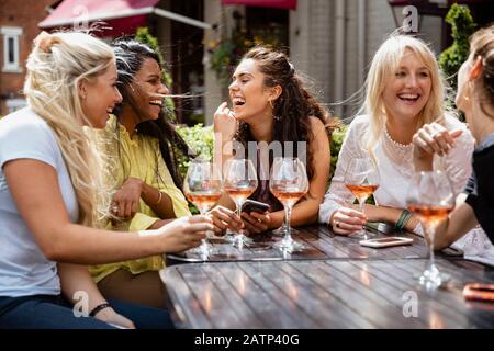 Eine Gruppe weiblicher Freunde, die im Sommer zusammen im Freien trinken und lachen. Stockfoto