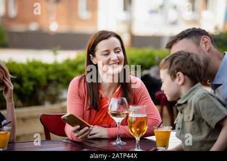 Eine Familie, die an einem Tisch im Freien sitzt und Getränke und Gespräche hat. Stockfoto
