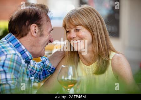 Ein älteres Paar, das sich umarmt, während es an einer Bar im Freien sitzt und Getränke bekommt. Stockfoto