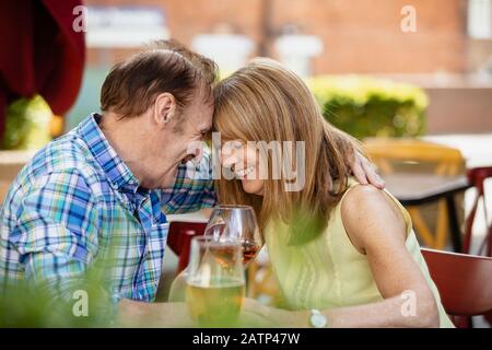 Ein älteres Paar, das sich umarmt, während es an einer Bar im Freien sitzt und Getränke bekommt. Stockfoto