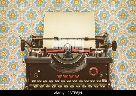 Retro-gestyltes Bild einer alten Schreibmaschine mit einem leeren Blatt Papier vor der Tapete mit Blumenmuster Stockfoto