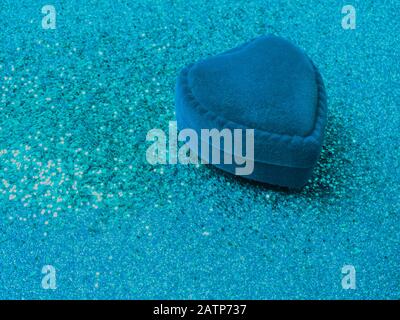 Herzförmige Ringbox aus blauem samt mit Glitzern auf trendig blauem Hintergrund. Geschenk für Valentinstag oder Geburtstag. Platz für Text kopieren Stockfoto