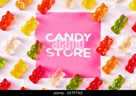 Flacher Laienblick auf bunte Gummibären-Bonbons mit einem Notizblatt, auf dem Süßwarenladen geschrieben ist. Stockfoto