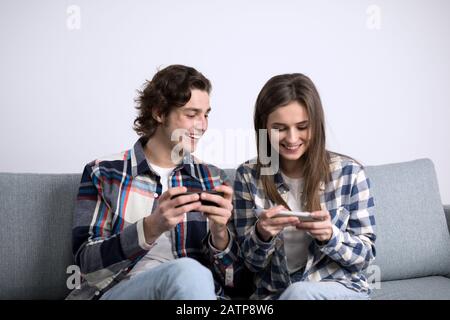 Fröhliches Paar lacht, während man Smartphones auf dem Sofa benutzt. Stockfoto