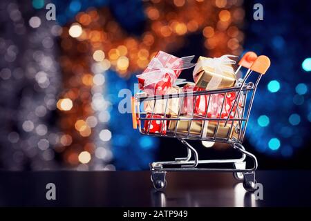 Einkaufswagen mit bunten Geschenkschachteln im Hintergrund der weihnachtsbeleuchtung. Konzept des Weihnachtseinkaufs. Stockfoto
