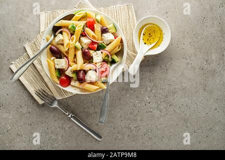 Nudelsalat mit Fetakäse und Gemüse auf grauem Hintergrund. Griechischen Salat mit Pasta. Stockfoto