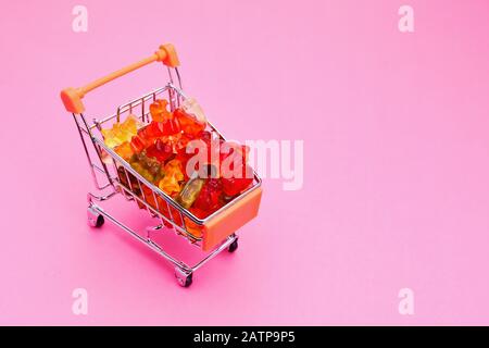 Einkaufswagen voller bunter Gummibären Süßigkeiten auf pinkfarbenem Hintergrund Stockfoto