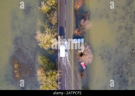 Das Bild vom 27. Januar zeigt ein Fahrzeug, das an Autos vorbeifährt, die bei den letzten Überschwemmungen auf der A1101 an der Grenze zu Cambridgeshire/Norfolk gefangen wurden und jetzt gerade sichtbar sind, nachdem das Hochwasser untergegangen ist. Das Hochwasser entlang eines berüchtigten Straßenabschnitts in Welney an der Grenze zu Cambridgeshire/Norfolk hat nachgelassen und enthüllt heute unglaubliche VIER gestrandete Autos (Mon). Die Autofahrer waren alle von dem seit zwei Monaten überschwemmten langen und kurvenreichen Straßenabschnitt erfasst. Vier Personen mussten von den Feuerwehrleuten aus einem der Autos gerettet werden, nachdem sie am Welney Wash auf Janu gefangen wurden Stockfoto