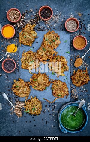 Hausgemachte Zwiebel-Bhajis mit Gewürzen auf Schiefergrund Stockfoto