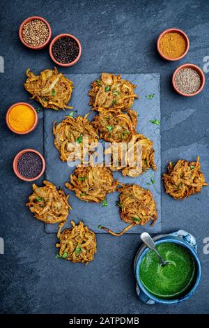 Hausgemachte Zwiebel-Bhajis mit Gewürzen auf Schiefergrund Stockfoto