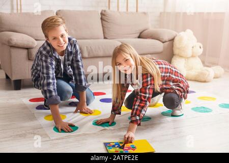 Fröhliche Geschwister, die Twister-Spiel auf dem Boden spielen und Spaß in der Halle haben Stockfoto