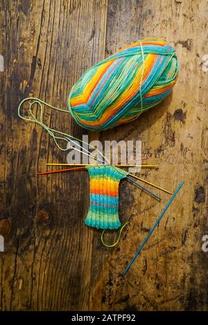 Blick auf bunte Wolle und Nadeln mit Socken, die auf einem rustikalen Holzhintergrund gestrickt sind Stockfoto