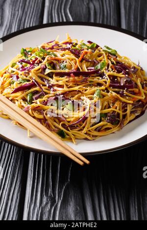 Asiatischer Noodle-Salat mit dünn geschnittenem Rotkohl, gebuhlte Karotten in würziger Erdnussdressing in einem Teller auf dem Tisch. Vertikal Stockfoto