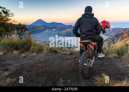 Ein Mann, der auf einem Motorrad sitzt, beobachtet den Sonnenaufgang in Bromo aus einem geheimen Blickwinkel, Bromo Tengger Semeru Nationalpark; Pasuruan, Ost-Java, Indonesien Stockfoto