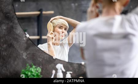 Happy Middle-Abged Lady, Die Haare Putzt Und Im Badezimmer Im Spiegel Sieht Stockfoto