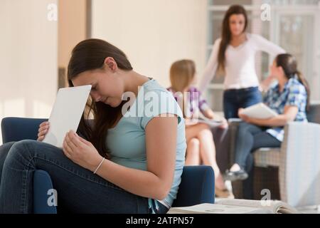 Teenager Mädchen mit Laptop in der Schule und versteckt den Bildschirm Von anderen mit zwei Studenten Blick auf Lehrbücher in der Hintergrund Stockfoto