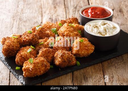 Portion Tiefgebratene Huhnnuggets in Kokosflocken, serviert mit Ketchup und Mayonnaise Nahaufnahme auf einem Schieferbrett auf dem Tisch. Horizontal Stockfoto