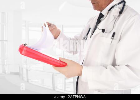 Nahaufnahme eines Arztes, der in einer modernen medizinischen Einrichtung steht. Der Mann hält einen Patienten in der Krankengeschichte und hält ein Diagramm in seinen Händen. Stockfoto