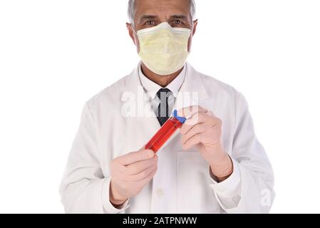Labortechniker, der eine Durchstechflasche mit roter Flüssigkeit vor seinem Körper hält. Der Mann trägt eine Schutzmaske, um eine Infektion zu verhindern. Stockfoto