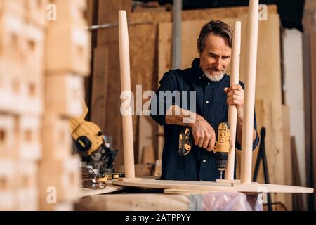 Zimmermann bohrt ein Loch in einem Holztisch an der Werkbank Stockfoto