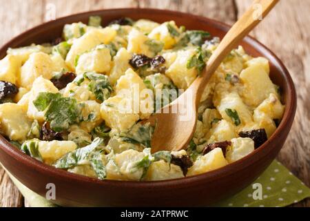 Kartoffelsalat mit Joghurt, Kräutern, Gewürzen und getrockneten Oliven wird in einer Schüssel auf dem Tisch serviert. Horizontal Stockfoto
